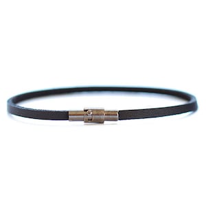 May include: A thin black leather bracelet with a silver clasp.