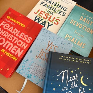 K&ouml;nnte beinhalten: Eine Sammlung von Hardcover-B&uuml;chern mit Titeln wie "Fearless Christian Women in History", "Raising Families the Jesus Way" und "Daily Devotion from Psalms". Die B&uuml;cher sind in verschiedenen Farben, darunter Rot, Blau und T&uuml;rkis.