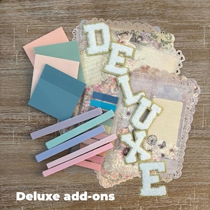K&ouml;nnte beinhalten: Eine Sammlung von Schreibwaren, darunter pastellfarbene Haftnotizen, Marker und dekoratives Papier. Das Wort "DELUXE" ist mit wei&szlig;en, flauschigen Buchstaben mit goldenem Rand geschrieben. Der Text "Deluxe add-ons" befindet sich unten.