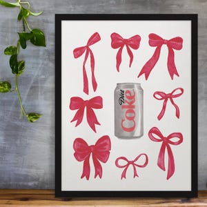 May include: A framed print featuring a Diet Coke can surrounded by watercolor illustrations of red bows. The bows vary in size and style, creating a playful and decorative design. The artwork is set against a white background.