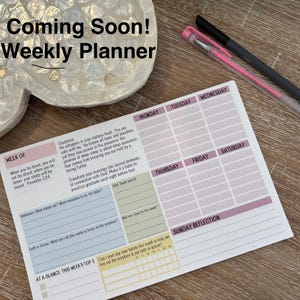 K&ouml;nnte beinhalten: Ein Wochenplaner mit dem Text "Coming Soon! Weekly Planner" oben. Der Planer hat Abschnitte f&uuml;r jeden Wochentag mit Platz f&uuml;r Notizen und Reflexionen. Ein rosa Stift und ein schwarzer Stift befinden sich auf der rechten Seite.