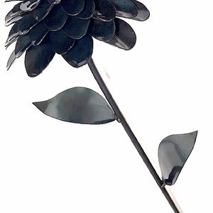 May include: A black metal flower with a single stem and leaves. The flower is made of many overlapping petals, giving it a full and rounded appearance.