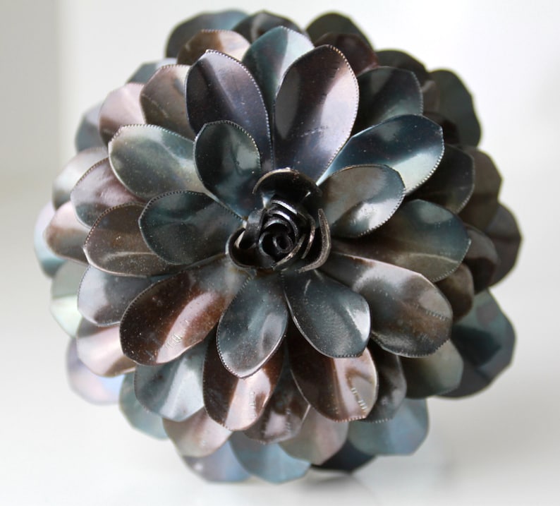 May include: A metal flower sculpture with iridescent blue and brown petals. The flower is made of many individual metal pieces that are layered to create a 3D effect.