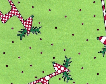 May include: Green fabric with a repeating pattern of reindeer with red and white polka dots and red and white checkered antlers. Small red dots are scattered across the background. The image includes a ruler with inch measurements.