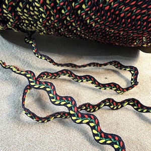 May include: A roll of navy blue trim with a colorful leaf pattern in red, yellow, and green. The trim is wavy and appears to be made of a woven material, suitable for sewing or crafting projects.