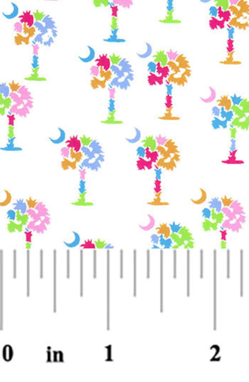 May include: White fabric with a repeating pattern of colorful palm trees and crescent moons. The fabric is measured with a ruler in inches.
