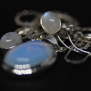 May include: A silver necklace with three oval-shaped moonstone pendants. The stones are iridescent and have a milky white color.