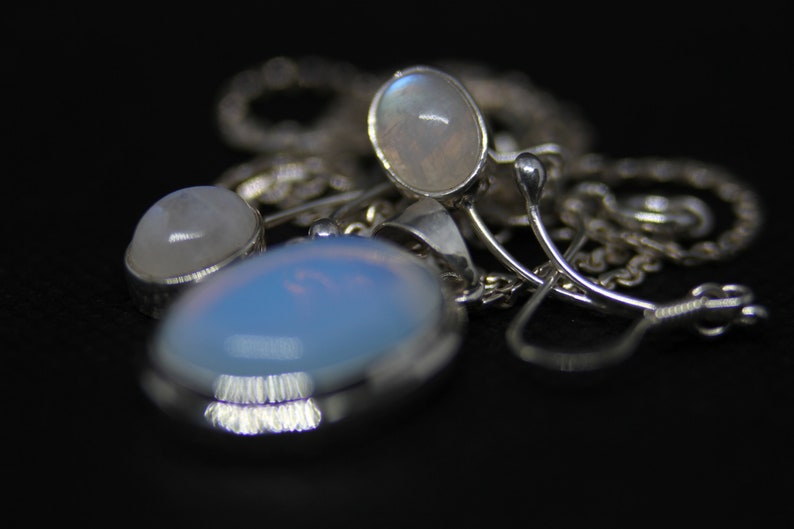 May include: A silver necklace with three oval-shaped moonstone pendants. The stones are iridescent and have a milky white color.