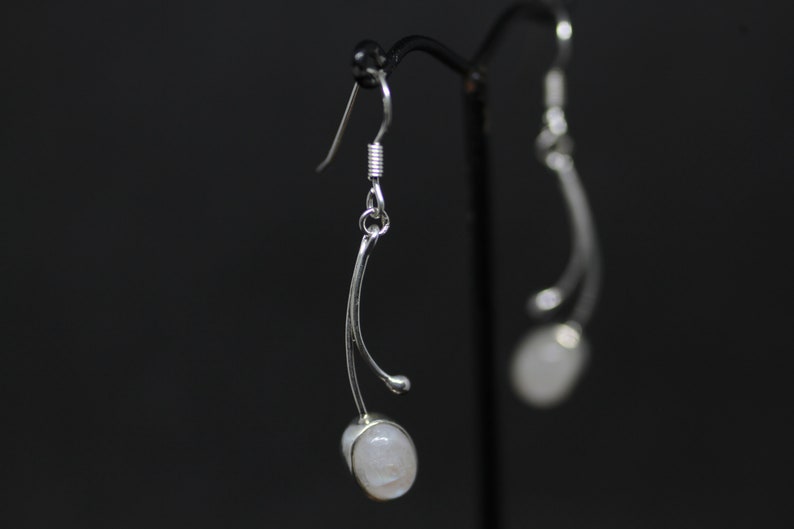May include: Silver dangle earrings with a white moonstone gemstone on each earring.