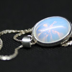 May include: A silver chain necklace with a pendant featuring a round, iridescent opal stone.