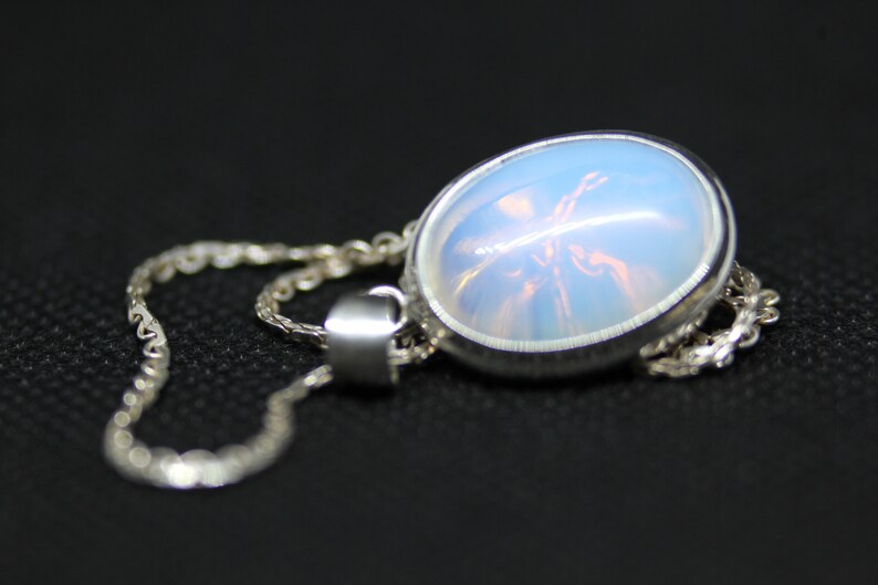 May include: A silver chain necklace with a pendant featuring a round, iridescent opal stone.