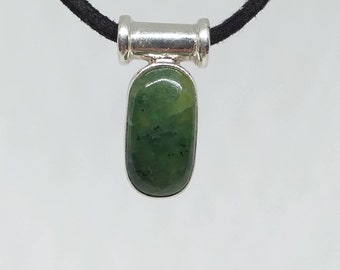 May include: A pendant necklace featuring a polished, green jade stone set in a silver-tone metal frame. The pendant hangs from a black cord. The jade stone has a smooth, rounded rectangular shape.