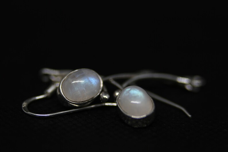May include: A pair of silver earrings with oval-shaped moonstone gemstones. The earrings have a simple design and are perfect for everyday wear.