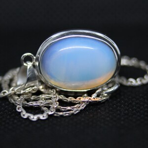 May include: A silver chain necklace with a pendant featuring a large oval-shaped opal gemstone. The opal is a pale blue color with a hint of white.