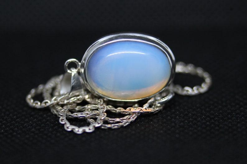 May include: A silver chain necklace with a pendant featuring a large oval-shaped opal gemstone. The opal is a pale blue color with a hint of white.