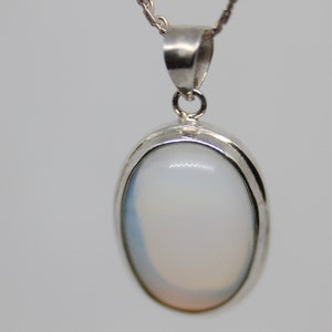 May include: A silver pendant with a white oval gemstone. The pendant has a simple design and is perfect for everyday wear.