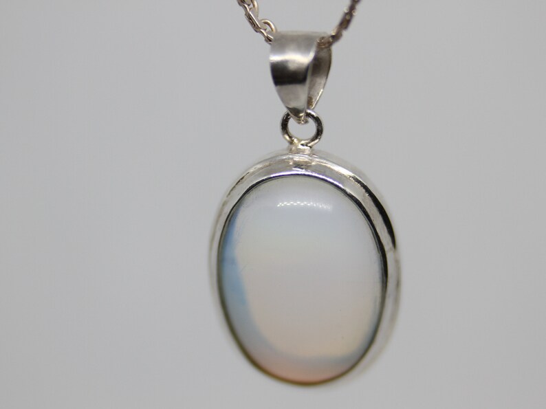 May include: A silver pendant with a white oval gemstone. The pendant has a simple design and is perfect for everyday wear.