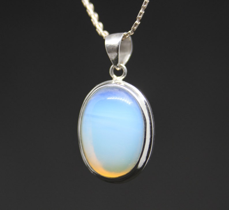 May include: A silver chain necklace with a pendant featuring a large oval-shaped opal gemstone. The opal is a light blue color with a hint of orange.