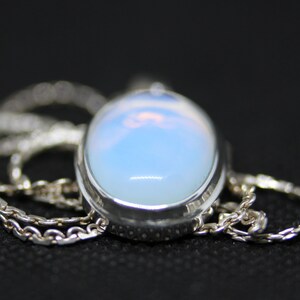 May include: A silver chain necklace with a large oval-shaped pendant featuring a milky white opal gemstone.