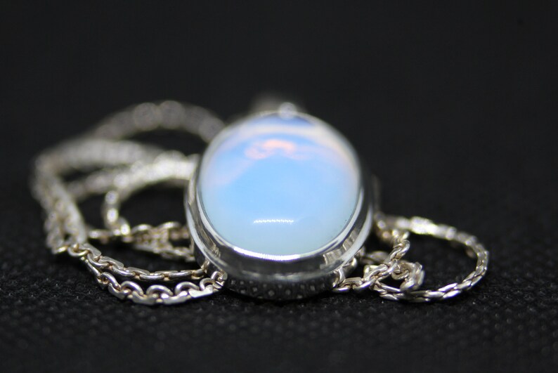 May include: A silver chain necklace with a large oval-shaped pendant featuring a milky white opal gemstone.