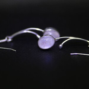 May include: A pair of silver earrings with a delicate, curved design and a pale pink oval gemstone.