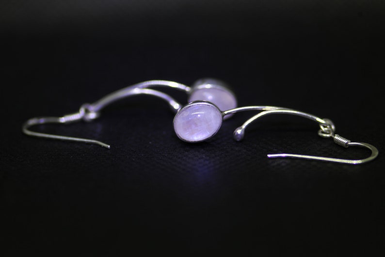 May include: A pair of silver earrings with a delicate, curved design and a pale pink oval gemstone.