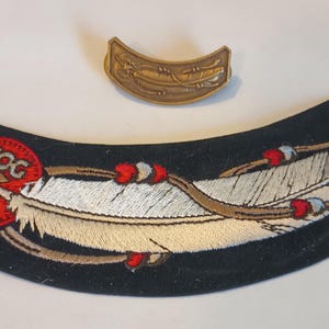 May include: Black embroidered patch with a white feather and red beads. The patch has a red circle with the text "HOG 2005" in white. A gold metal bar with a Harley Davidson logo is also included.