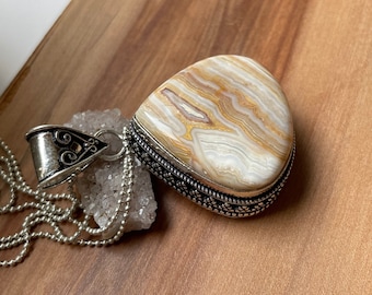 May include: A silver chain necklace with a pendant featuring a large, teardrop-shaped, brown and white agate stone with a silver filigree border.