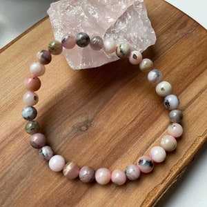 Peut inclure: Un bracelet en opale rose avec des nuances de rose, blanc et gris. Le bracelet est composé de perles rondes et est monté sur un élastique.