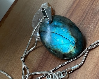 May include: A silver chain necklace with a large oval-shaped labradorite pendant. The pendant has a blue, green, and black iridescent sheen.