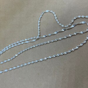May include: A silver chain necklace with a twisted design. The chain is layered on itself, creating a thick and textured look.