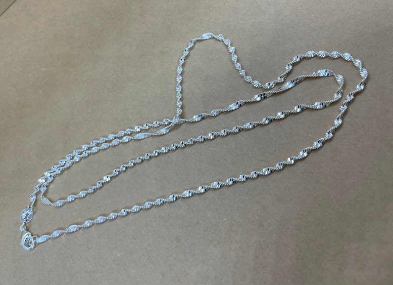 May include: A silver chain necklace with a twisted design. The chain is layered on itself, creating a thick and textured look.