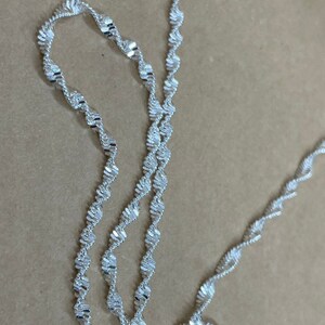 May include: A silver chain necklace with a twisted design. The chain is made of small, flat links that are woven together to create a unique and stylish look.