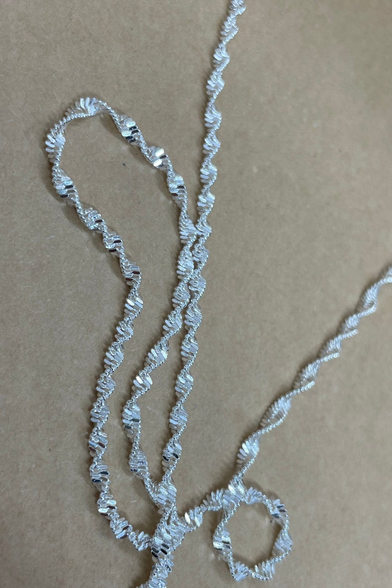 May include: A silver chain necklace with a twisted design. The chain is made of small, flat links that are woven together to create a unique and stylish look.