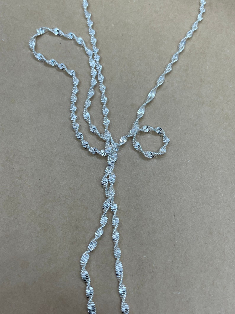 May include: A silver chain necklace with a twisted design. The chain is made of small, linked metal pieces.
