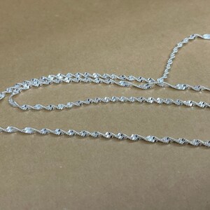 May include: A silver chain necklace with a twisted design. The chain is made of multiple strands of silver wire that are twisted together to create a rope-like effect.
