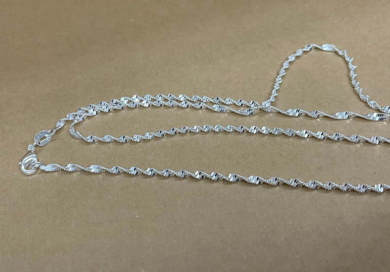 May include: A silver chain necklace with a twisted design. The chain is made of multiple strands of silver wire that are twisted together to create a rope-like effect.
