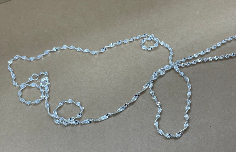 May include: A silver chain necklace with a twisted design. The chain is about 20 inches long.