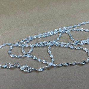 May include: A silver chain necklace with a twisted design. The chain is approximately 20 inches long.