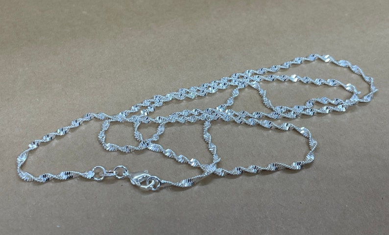 May include: A silver chain necklace with a twisted design. The chain is approximately 20 inches long.