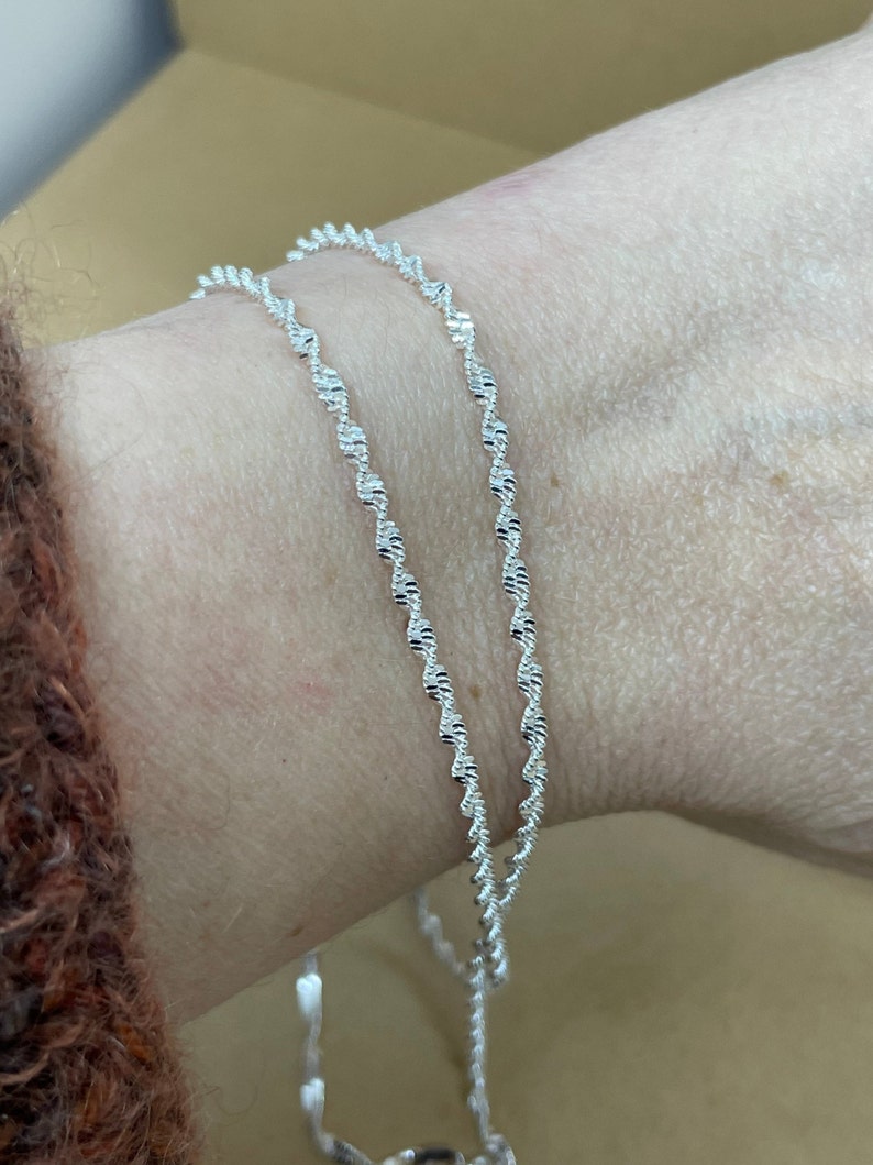 May include: Two silver chains with a twisted design, worn on a wrist.