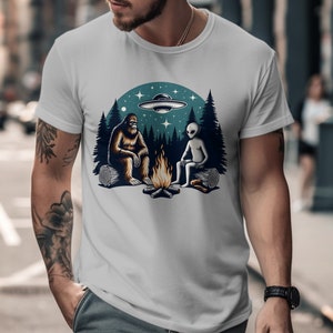 Lustiges Lagerfeuer mit Lagerfeuer, Sasquatch und Alien Shirt, UFO Waldnachthimmel, Galaxie Abenteuer Grafik-T-Shirt