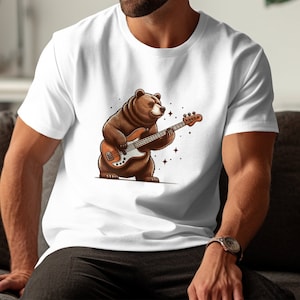 May include: A white t-shirt with a brown bear playing a bass guitar. The bear is wearing a brown fur coat and has a black nose and eyes. The bass guitar is brown and has a white pickguard. The background is white with a few small stars.