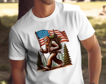 Puede incluir: Una camiseta blanca con un gráfico de un Bigfoot llevando una mochila y una bandera estadounidense. El Bigfoot camina por un bosque.