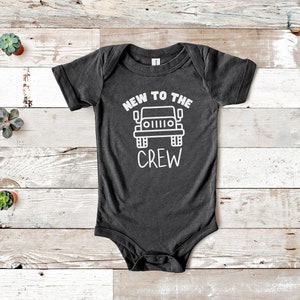 Könnte beinhalten: Ein dunkelgrauer Baby-Strampler mit weißem Text, der "New to the Crew" lautet, und einer weißen Umrandung eines Jeeps.