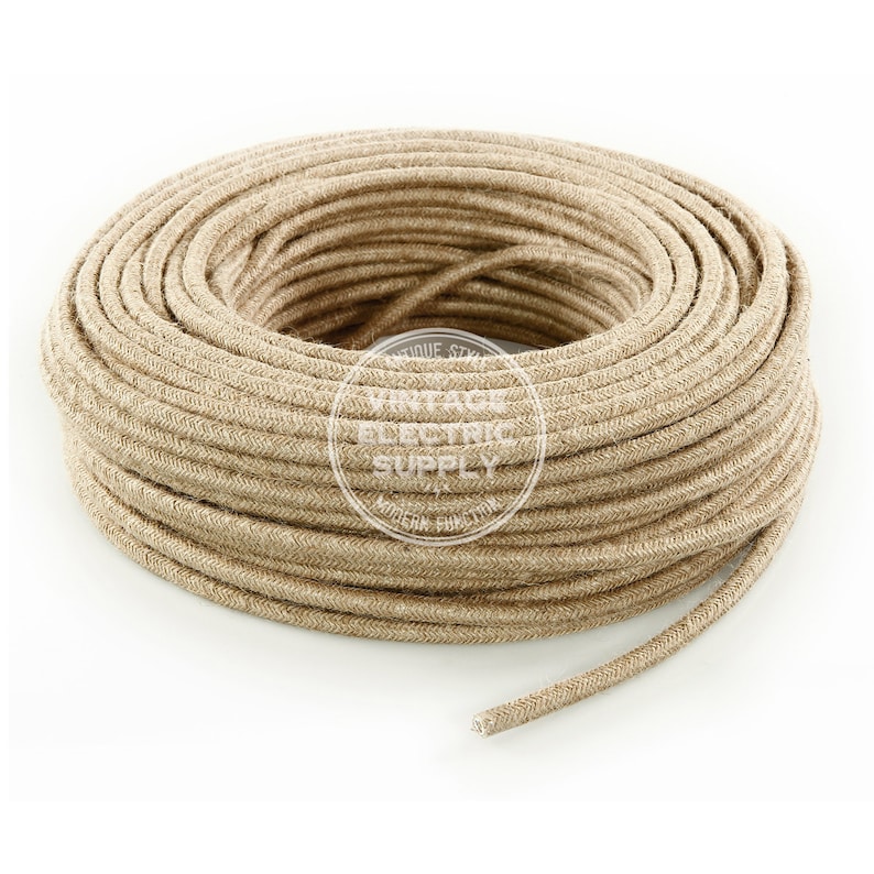 Puede incluir: Un primer plano de un carrete de cord&oacute;n de lino natural, envuelto en espiral. El cord&oacute;n es de color beige claro y tiene un aspecto texturizado y tejido. El carrete est&aacute; etiquetado como "Vintage Electric Supply".