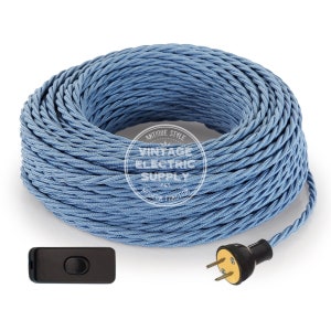Puede incluir: Una bobina de cable eléctrico trenzado azul claro con un interruptor en línea negro y un enchufe negro con clavijas doradas. El cable está etiquetado como "Antique Style Vintage Electric Supply".