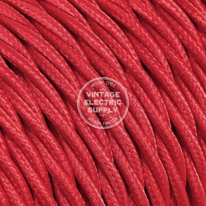 Puede incluir: Primer plano de un cable eléctrico rojo con una superficie texturizada. El cable está retorcido y enrollado. El texto "Antique Style Vintage Electric Supply Modern Function" es visible en un círculo blanco.
