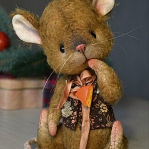 Op de afbeelding: Een bruine pluche muis die een bruin vest met bloemenprint en een bruin lint draagt. De muis heeft een lange staart en zit op een wit oppervlak.
