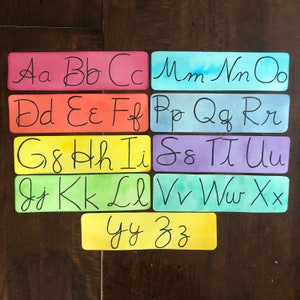 Könnte beinhalten: Ein Satz bunter Alphabet-Karteikarten mit Aquarellhintergründen. Jede Karte zeigt einen Buchstaben des Alphabets in Kursivschrift. Die Buchstaben sind in alphabetischer Reihenfolge angeordnet.